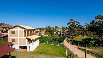 A two-story building with a flat roof and a balcony, surrounded by a fenced yard and a dirt road.