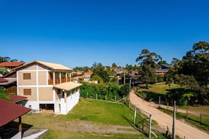 A two-story building with a flat roof and a balcony, surrounded by a fenced yard and a dirt road. - House w/ Priv. Jacuzzi & Mtn. View Tst001 (Florianópolis)
