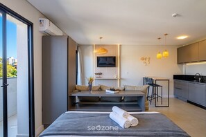 A modern hotel room with a sofa, a TV, a dining area, and a kitchen. - Apt. w/ AC in Trindade, Floripa Tst001 (Florianópolis)
