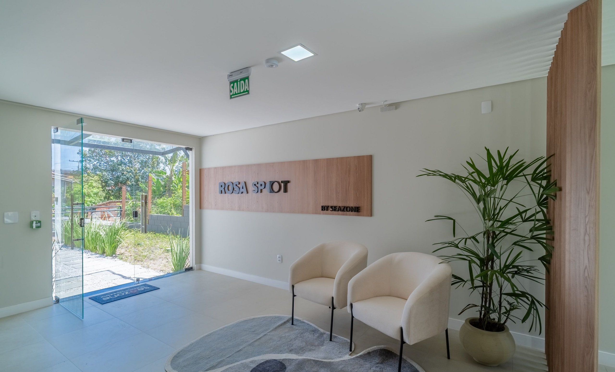 A modern interior with a reception desk, two chairs, a large wooden sign, and a potted plant.