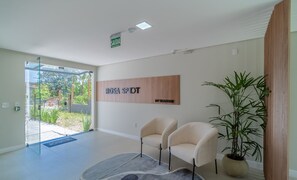 Un interior moderno con un mostrador de recepción, dos sillas, un gran letrero de madera y una planta en maceta.