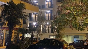 Un edificio de varios pisos con balcones, una tienda visible en la planta baja y coches aparcados.