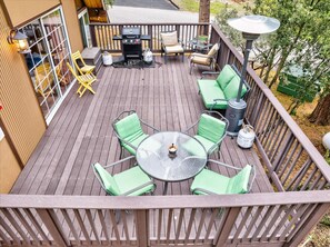 Une terrasse en bois avec une table ronde en verre et des chaises vertes, entourée d’une rambarde.