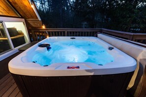 Un bain à remous installé sur une terrasse extérieure, dotée d’une rambarde en bois et d’une fenêtre.