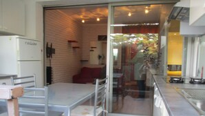 Una cocina con refrigerador, una mesa, sillas y una puerta de vidrio que da a un comedor.