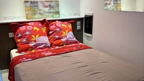 Un dormitorio con cama, almohadas, una mesita de noche, un espejo y obras de arte en la pared.