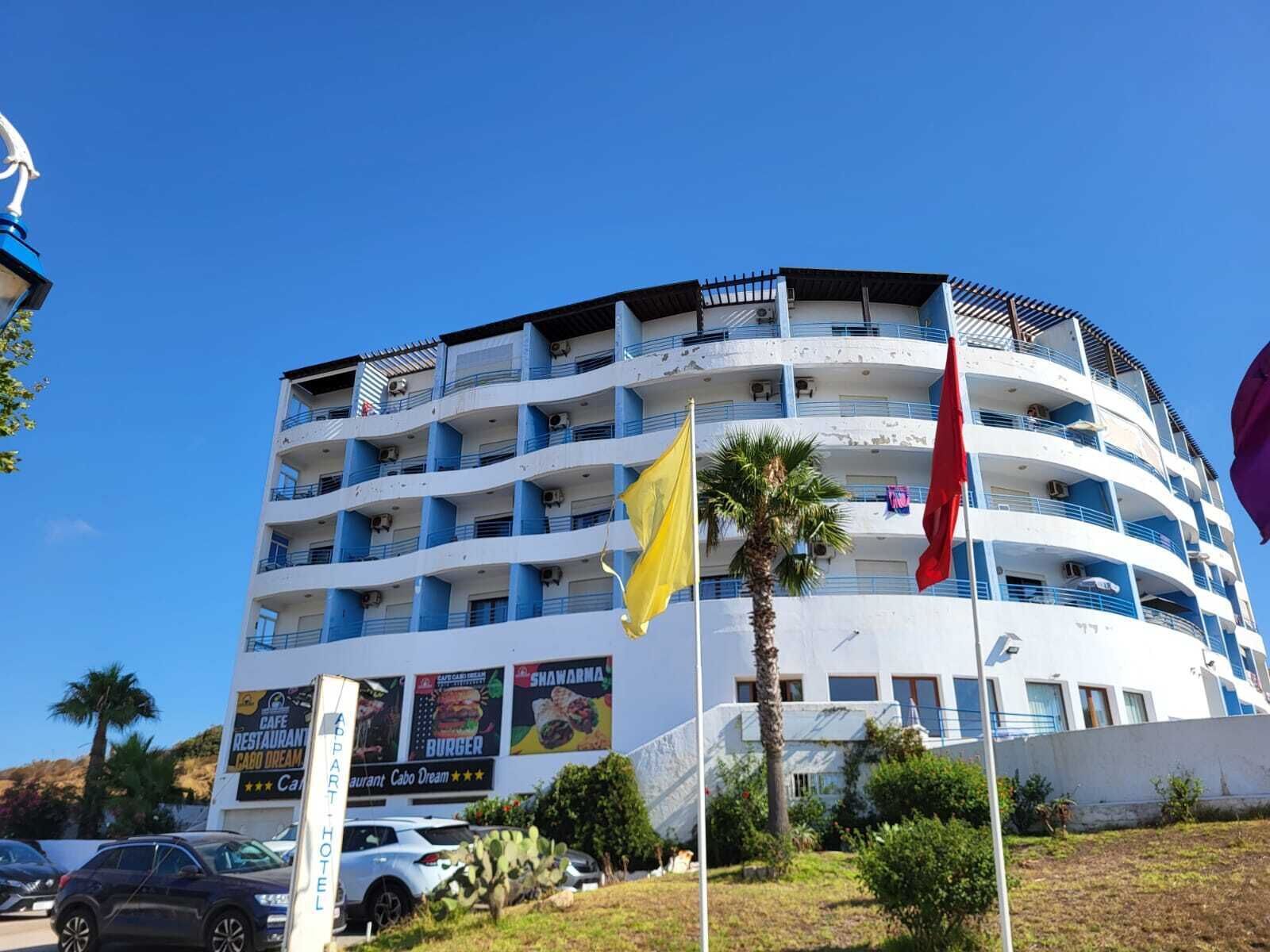 A multi-story hotel with balconies, a palm tree, and flags.