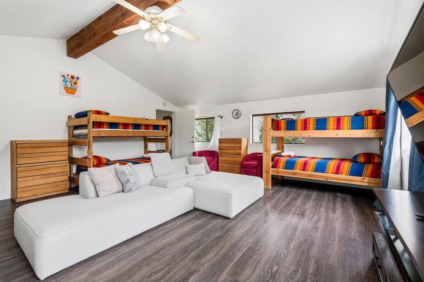 Una habitación con literas, un sofá blanco, un armario de madera y un ventilador de techo.