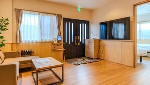 Une chambre d’hôtel avec un plancher en bois, un canapé, une table basse, une télévision et un lit.