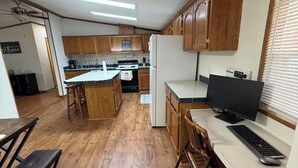 A kitchen with wooden cabinets, a central island, a dining area with a bench, and a computer setup.