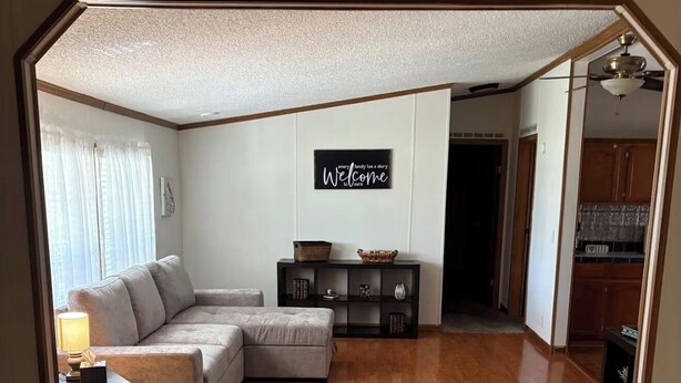 A living room with a sectional sofa, a small table with a lamp, a decorative wall sign, and a wooden floor.