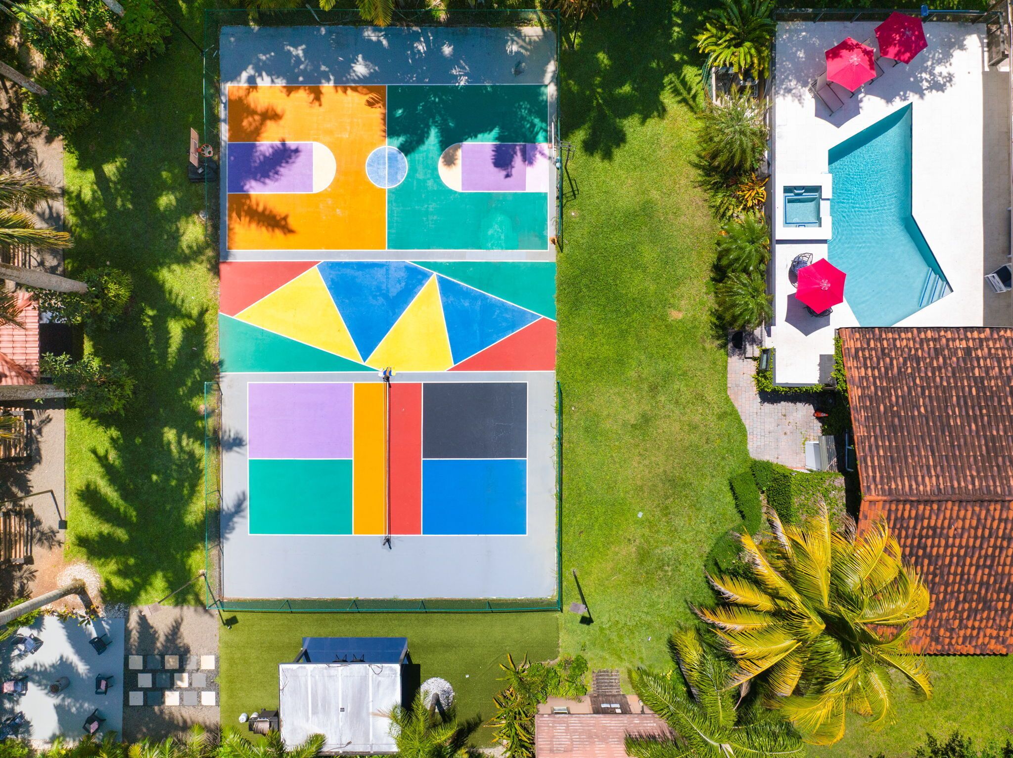 An aerial view of a property with a colorful outdoor area, a swimming pool, and a tiled roof.