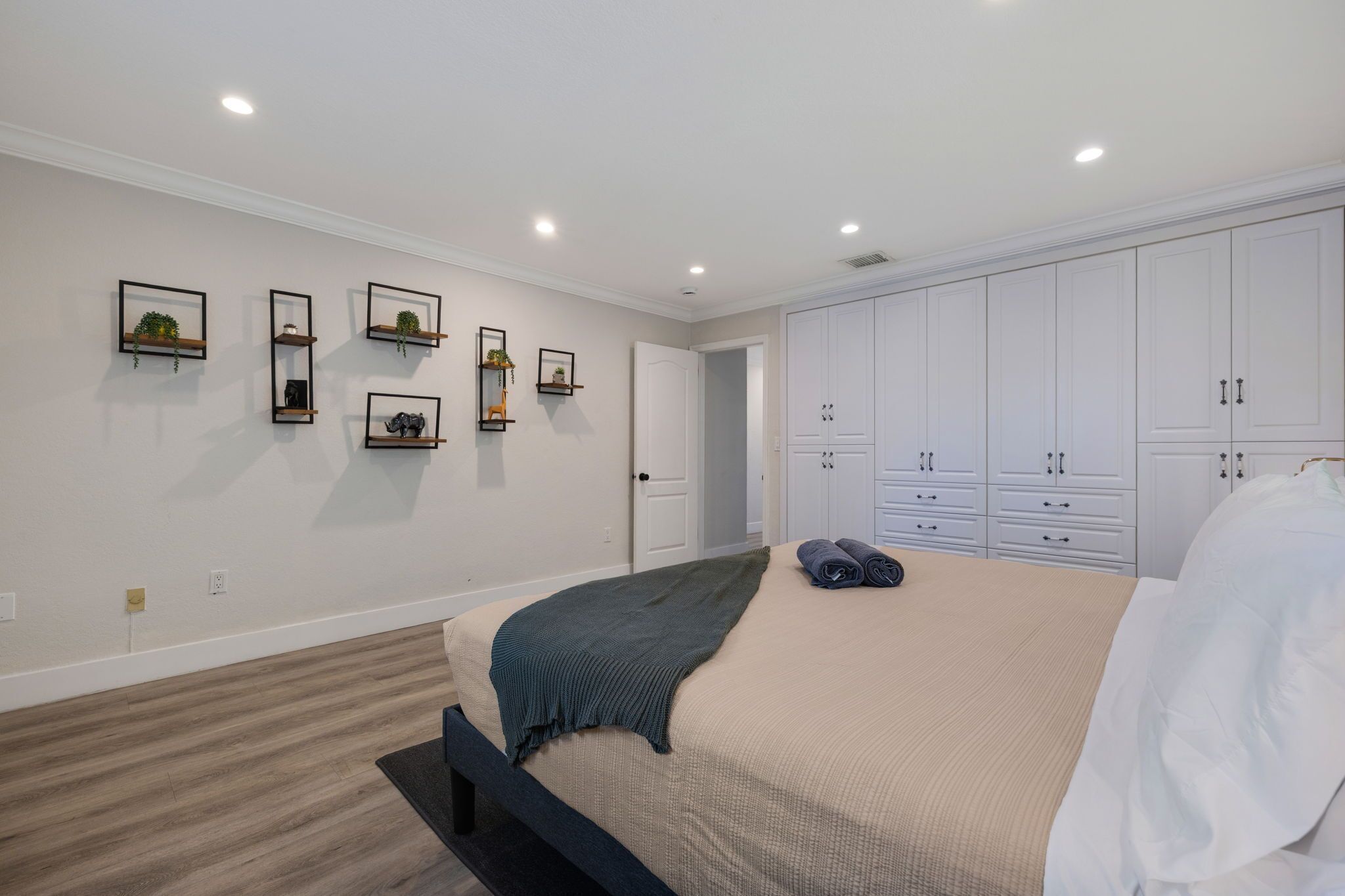 A bedroom with a bed, a wardrobe, and wall-mounted shelves with decorative items.