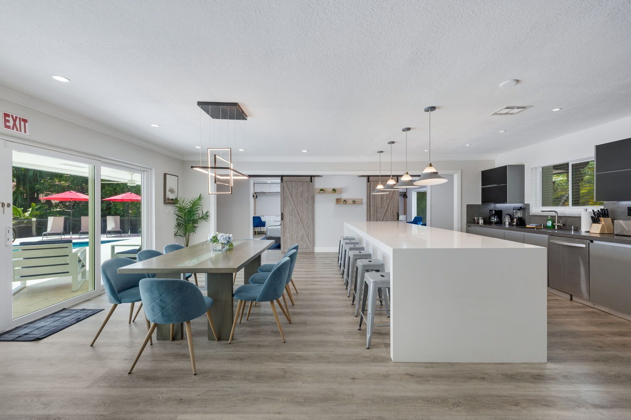 A modern kitchen with a central island, bar stools, and a dining area with blue chairs.