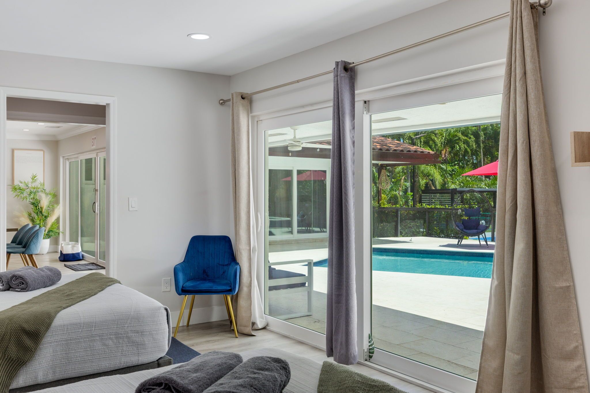 A hotel room with a bed, a blue chair, a pool view, and a sliding glass door.