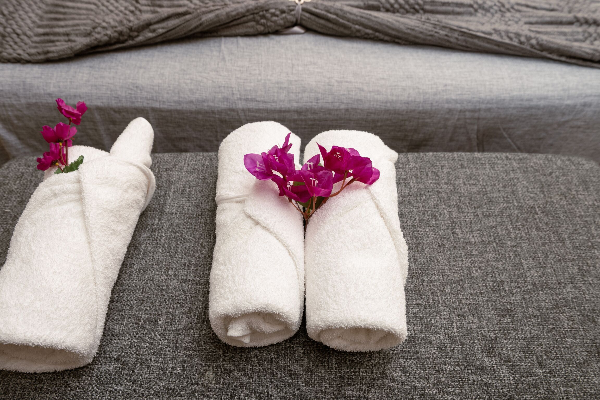 Two white towels with purple flowers on a grey sofa.