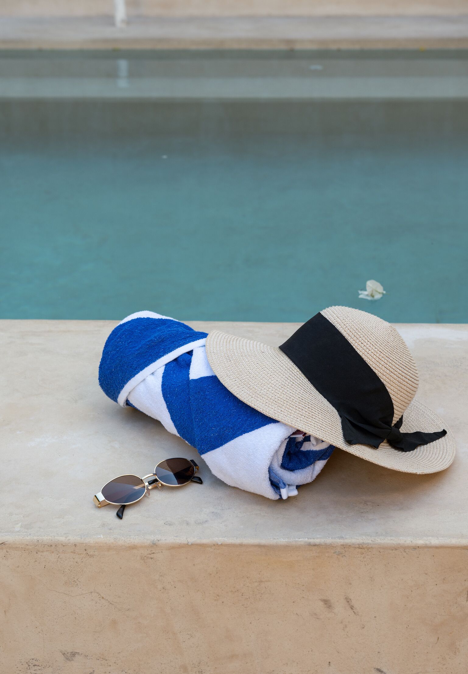 Ein Handtuch, Sonnenbrille und Hut liegen auf einem Betonvorsprung an einem Pool.