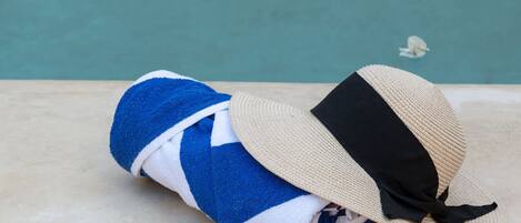 Ein Handtuch, Sonnenbrille und Hut liegen auf einem Betonvorsprung an einem Pool.