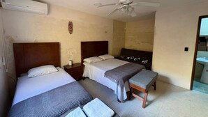 Quarto com duas camas, ventilador de teto e banheiro à vista.