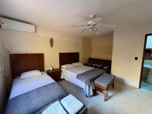 Habitación con dos camas, ventilador de techo y baño a la vista.