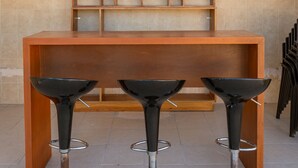 Uma área de bar com balcão de madeira e três banquetas pretas.