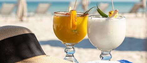 Two drinks on a beach towel, a hat, and sunglasses.