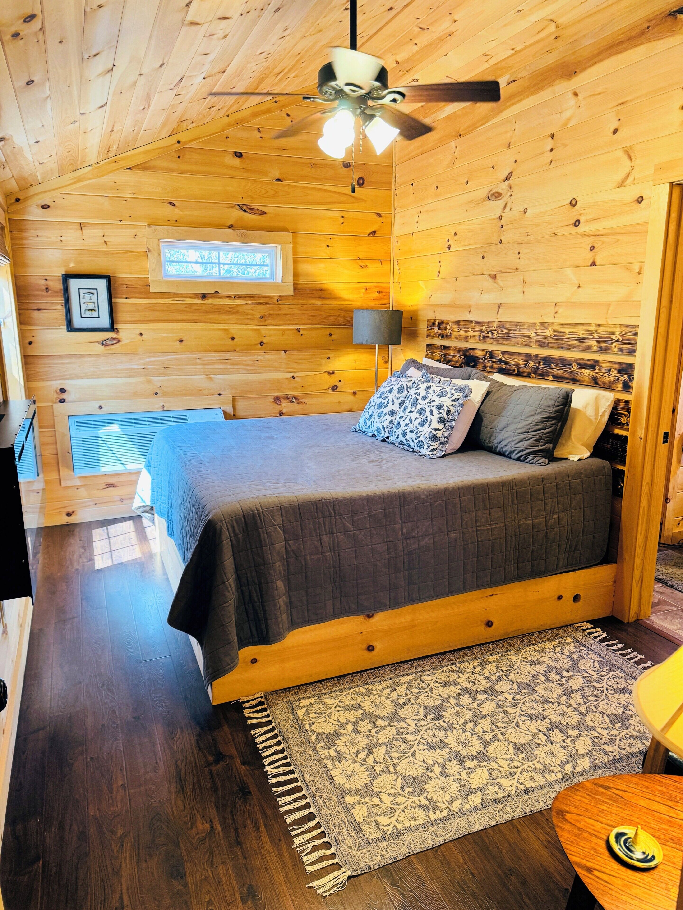Dormitorio de cabaña de madera con cama, ventilador de techo y ventana.