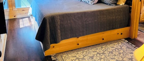 Dormitorio de cabaña de madera con cama, ventilador de techo y ventana.
