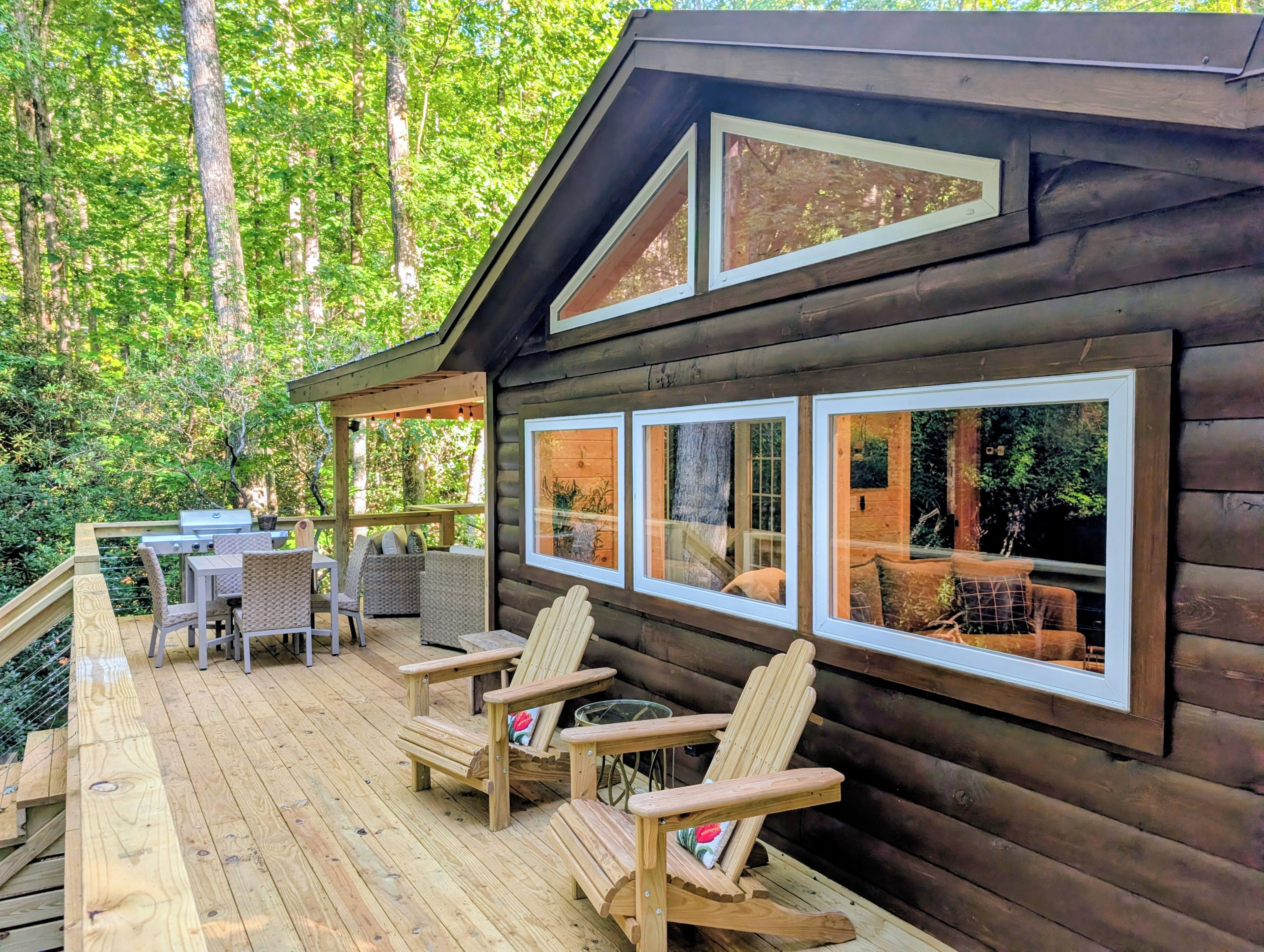 A wooden cabin with a deck, outdoor seating, and large windows.