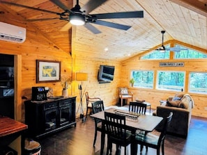 A cabin interior with a dining area, a sofa, and a TV mounted on the wall. - Cozy Cabin Near Lake Burton Clayton - Dog Friendly! (Clarkesville)