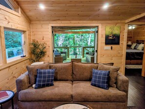 A wooden cabin interior with a sofa, a window, and a view of the outdoors.