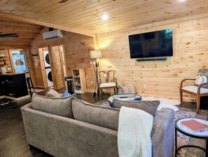 A cozy cabin interior with a sofa, chairs, a TV, and a washing machine.