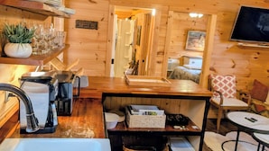 A wooden cabin interior with a kitchen area, a dining table, a TV, and a cozy bed. - Cozy Cabin Near Lake Burton Clayton - Dog Friendly! (Clarkesville)