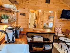 A wooden cabin interior with a kitchen area, a dining table, a TV, and a cozy bed.