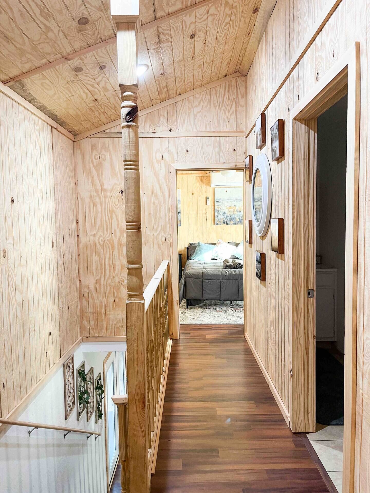 A wooden interior with a staircase, a bed in the background, and a circular mirror on the wall.