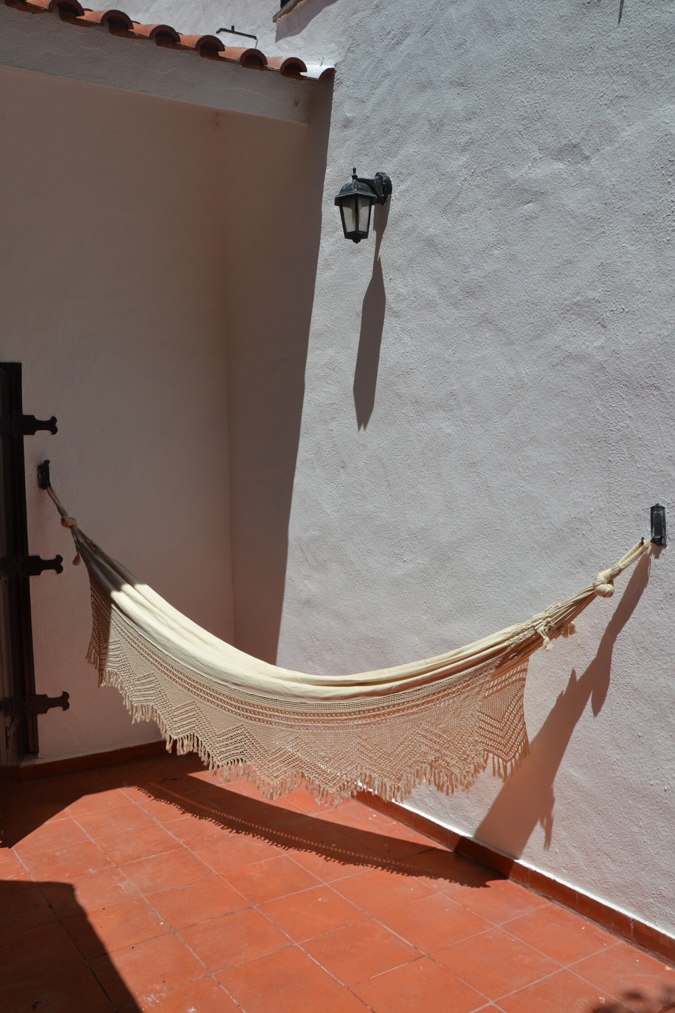 A hammock tied between two walls with a textured surface, a door frame, and a tiled floor.