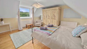 A bedroom with a sloped ceiling, a bed with a patterned blanket, a wooden wardrobe, a bedside table, and a view of greenery outside. - Private Loch-side escape in the Scottish highlands (Oban)
