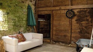 A rustic room with a white sofa, a dartboard, and a wheelbarrow. - Private Loch-side escape in the Scottish highlands (Oban)
