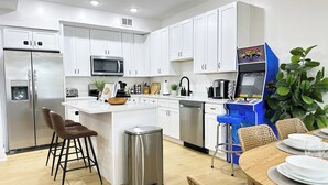 Una cucina moderna con mobili bianchi, un frigorifero in acciaio inossidabile, un forno a microonde e una macchina da caffè. È presente un'area pranzo con un tavolo in legno e sedie in vimini.