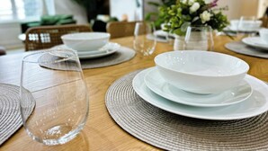 Un tavolo da pranzo apparecchiato con piatti bianchi, bicchieri trasparenti e un sottopiattino intrecciato.