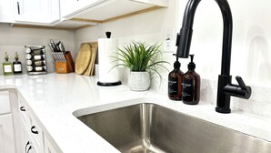 Una cucina con lavello in acciaio inox, un rubinetto nero e due flaconi di sapone per le mani sul piano di lavoro.