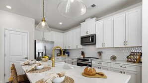 A modern kitchen with white cabinetry, a central island, a stainless steel refrigerator, and a microwave. - Hill Street Villa 2608 (North Myrtle Beach)