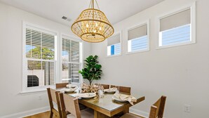 A dining room with a wooden table, chairs, a chandelier, and a potted plant. - Hill Street Villa 2608 (North Myrtle Beach)