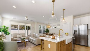 A modern kitchen with a central island, stainless steel appliances, and a seating area with a sofa and coffee table. - Hill Street Villa 2608 (North Myrtle Beach)