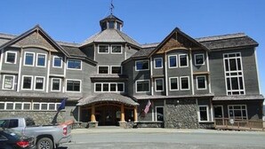 A large, multi-story building with a prominent central entrance, stone foundation, and a flag. - Inn at Whittier (Whittier)