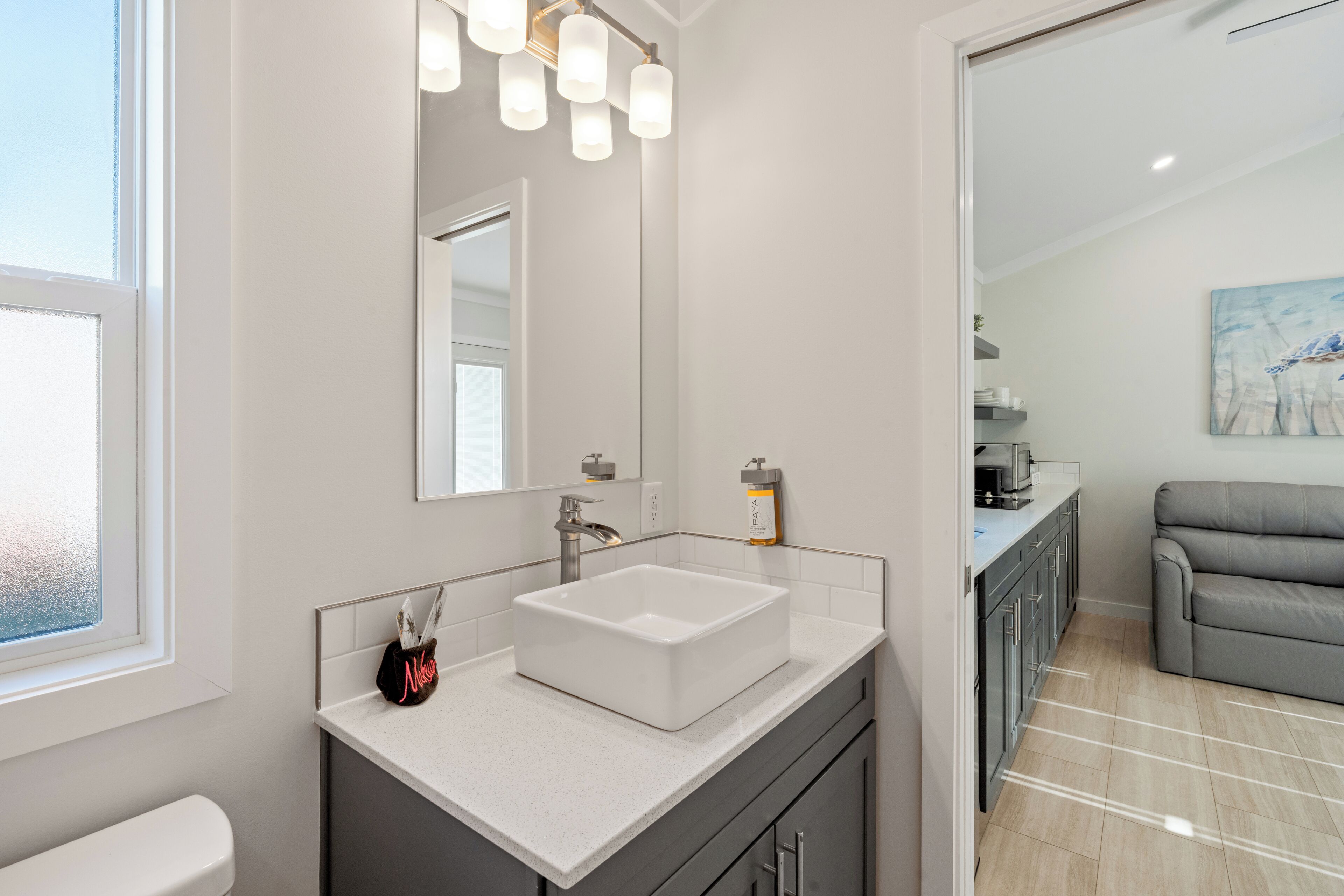 Un baño moderno con un lavamanos blanco, un espejo y una ventana.