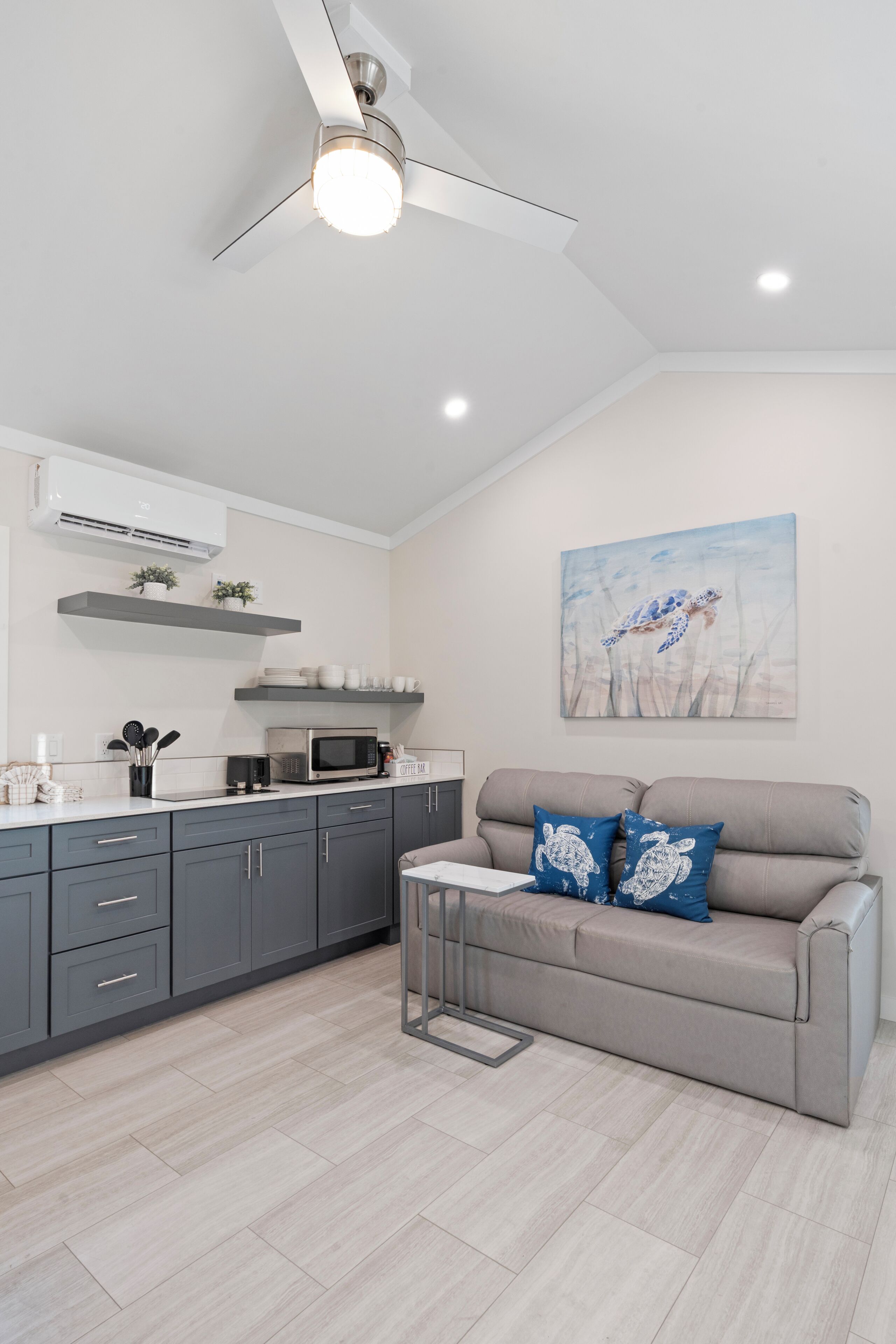 A modern kitchen with grey cabinets, a microwave, and a ceiling fan.
