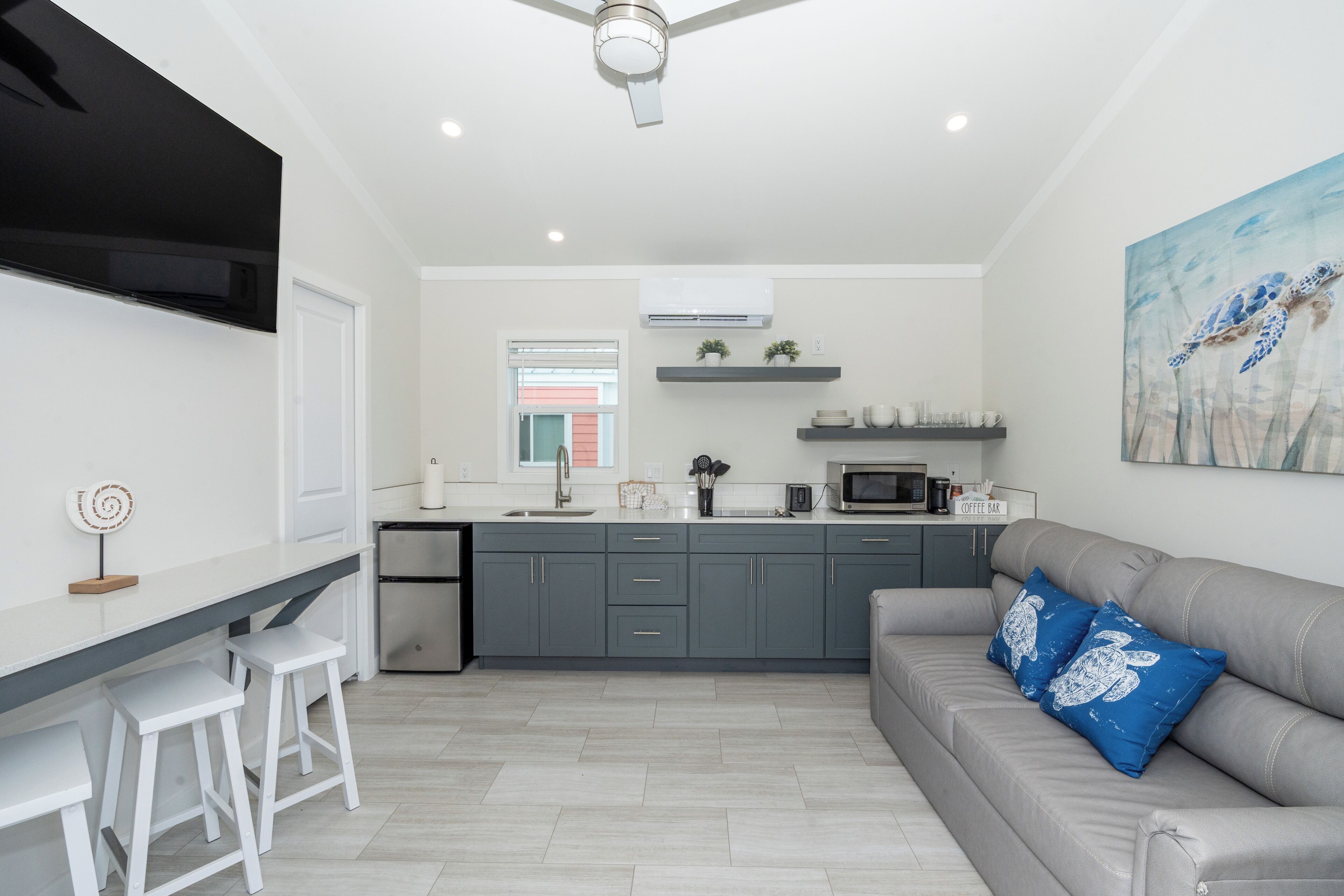 A modern kitchen with grey cabinets, a grey sofa, and a painting of a sea turtle.