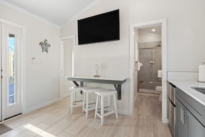 Una cocina moderna con televisor, taburetes blancos y zona de ducha.