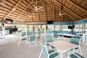 An outdoor dining area with thatched roof, white metal chairs, and tables.